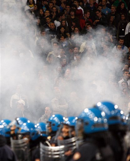 
 Spectators look on from behind smoke blowing from a flare and Italian police confront Serbia fans, not pictured, prior to the start of a Group C, Euro 2012 qualifying soccer match between Italy and Serbia, at the Luigi Ferraris stadium in Genoa, Italy, Tuesday, Oct. 12, 2010. The Italy-Serbia European Championship qualifier was called off after seven minutes of play on Tuesday after Serbia fans threw flares and fireworks onto the pitch. (AP Photo/Antonio Calanni)
 