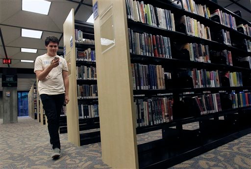 
 Hillard Goodspeed walks by rows of books as he uses an ipod application called 'shake it', to find reading suggestions at the Orlando Public Library in Orlando, Fla., Wednesday, Sept. 1, 2010.(AP Photo/John Raoux)
 