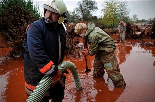 
 Hungarian fire fighters clean a yard flooded by toxic mud in Devecser, Hungary, Wednesday, Oct. 6, 2010. Monday's flooding was caused by the rupture of a red sludge reservoir at an alumina plant in western Hungary and has affected seven towns near the Ajkai, 100 miles (160 kilometers) southwest of Budapest. The flood of toxic mud killed a yet unknown number of people, injured more than one hundred, with some people still missing. (AP Photo/Bela Szandelszky)
 