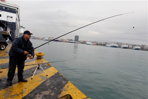 
 A man fishes at Piraeus port as at the background are seen docked vessels during a 24-hour strike, on Wednesday, Dec. 15, 2010. A general strike hit Greece Wednesday, grounding flights and disrupting hospital and transport services as unions protest against the freshly approved labor reforms amid painful austerity and rising unemployment. (AP Photo/Petros Giannakouris)
 
