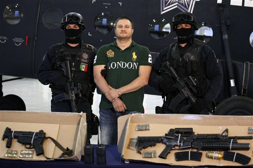 
 Federal police stand guard by Texas-born fugitive Edgar Valdez Villarreal, alias 'the Barbie,' center, as he is presented to the press along with weapons allegedly seized during his arrest in Mexico City, Tuesday Aug. 31, 2010. Valdez, the third major suspected drug lord to fall in Mexico in the past 10 months, is wanted in the United States for allegedly smuggling tons of cocaine and inside Mexico and is blamed for a brutal turf war that has included bodies hung from bridges, decapitations and shootouts as he and a rival fought for control of the divided Beltran Leyva cartel. (AP Photo/Alexandre Meneghini)
 